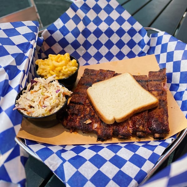 BBQ ribs with a slice of white bread, mac and cheese, and coleslaw in a checkered basket.