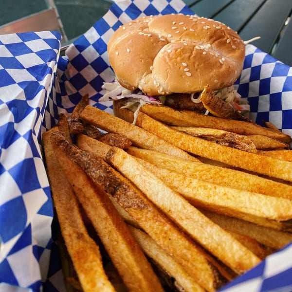 A burger with coleslaw and a side of seasoned fries in a blue and white checkered basket.