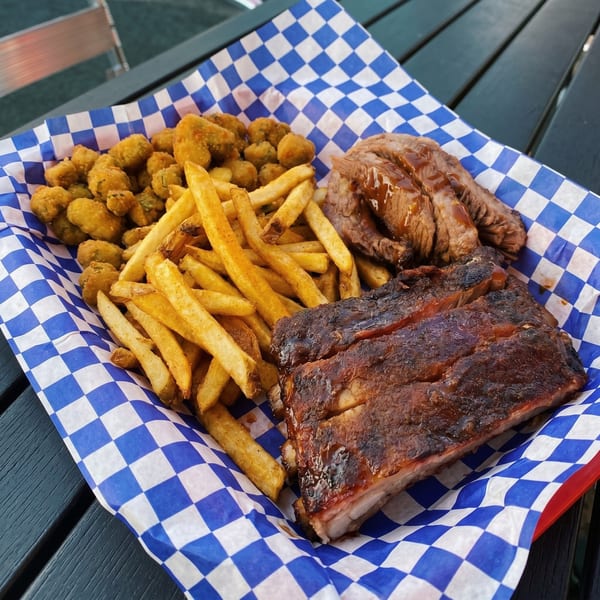 A basket of BBQ ribs, sliced brisket, french fries, and fried okra on blue and white checkered paper.