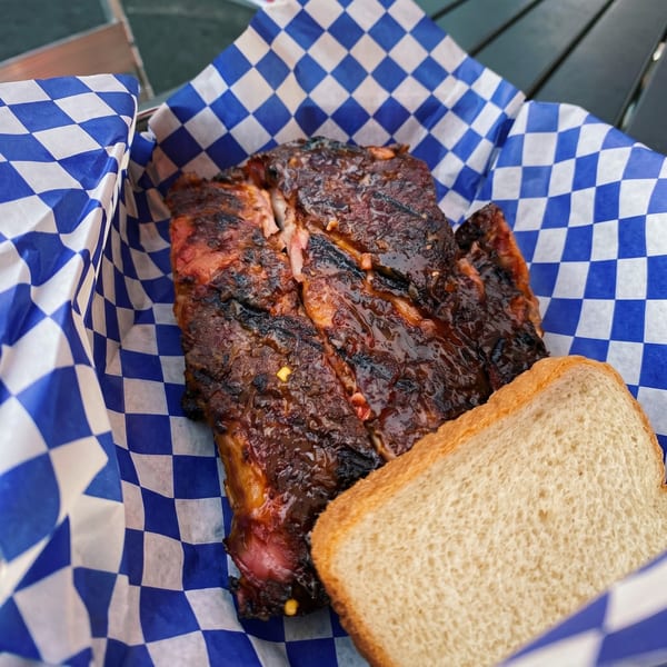 Barbecue ribs with sauce and a slice of white bread in a blue and white checkered basket.