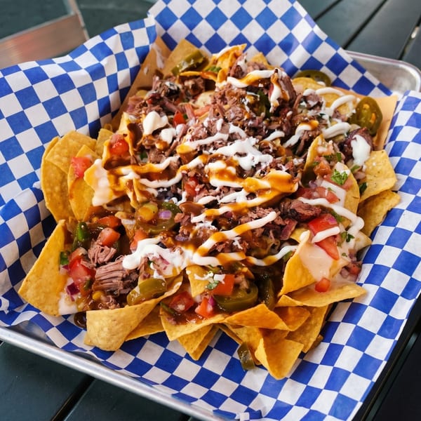 Loaded nachos with shredded beef, cheese sauce, jalapeños, and pico de gallo in a blue checkered basket.
