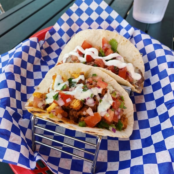 Two tacos with meat, pico de gallo, and sour cream in a blue and white checkered basket.
