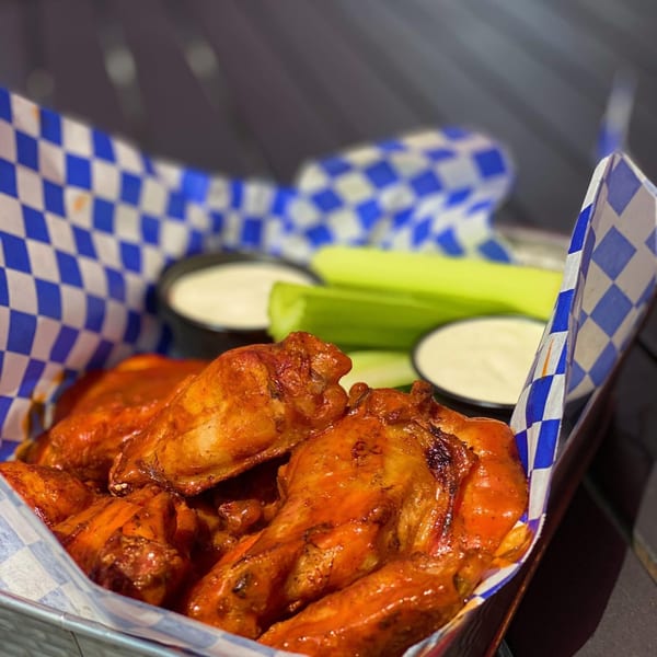 Buffalo chicken wings in a checkered basket with celery sticks and two dipping sauces.