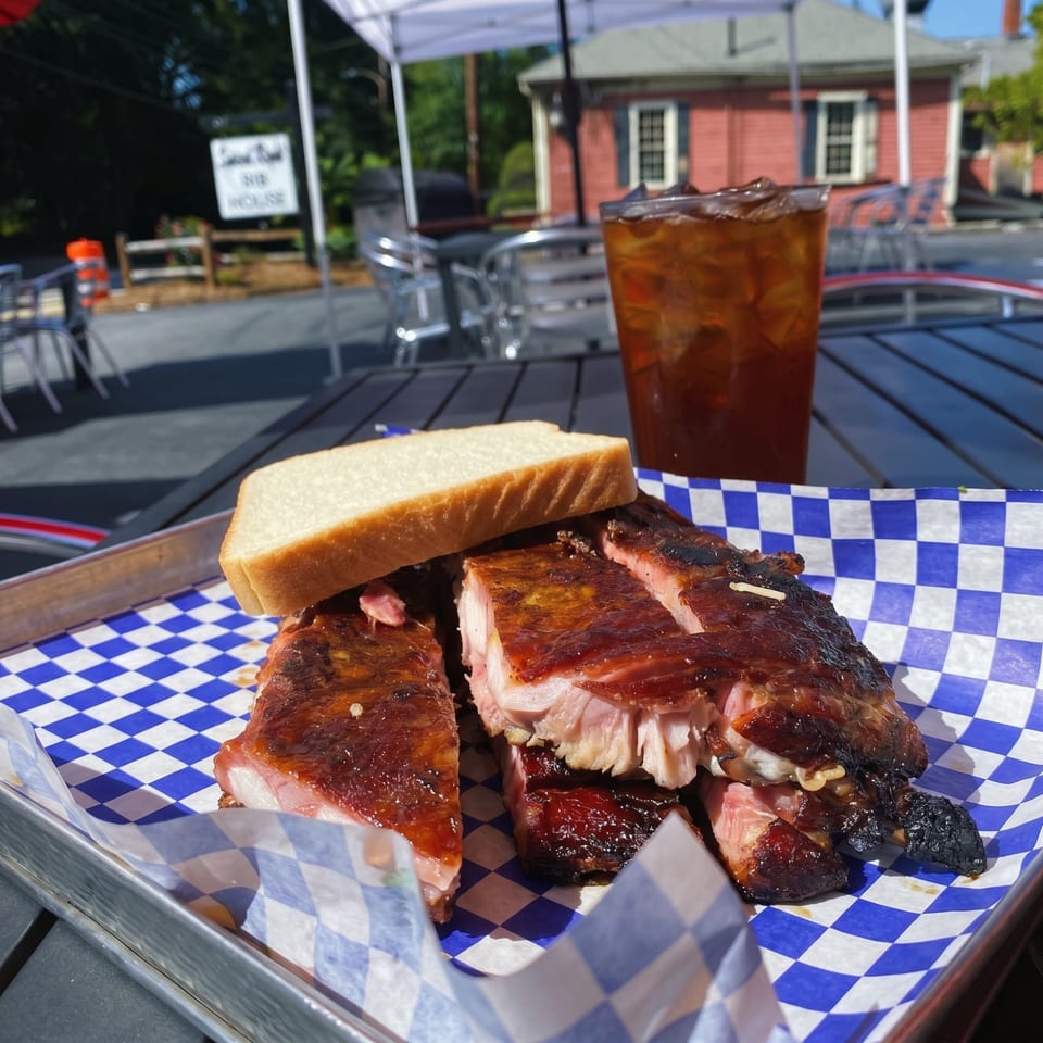 Sweet Rib House ribs with white bread and iced tea on a blue checkered tray outdoors.