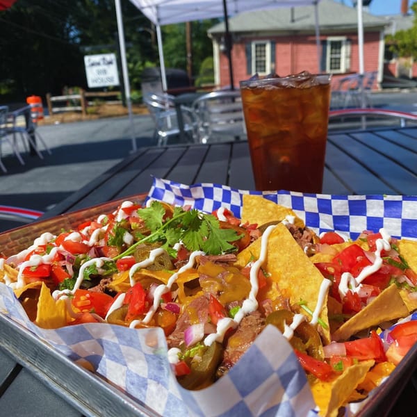 Loaded nachos with meat, cheese, salsa, and sour cream, next to an iced tea on an outdoor patio.
